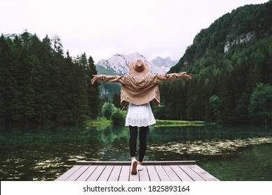 Young girl enjoying beauty of nature looking at mountain lake in Jezersko. Adventure travel in Slovenia, Europe. Woman stands with raised arms on wooden bridge on background with forest and Alps. - Powered by Shutterstock