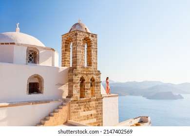Young girl enjoying breathtaking sunset view from atop of Greek Orthodox church in Plaka village on Milos island