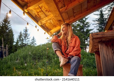 A young girl is enjoying the view from cottage porch in the forest on a beautiful evening. Vacation, nature, cottage
