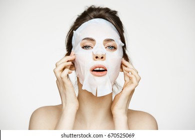Young girl with facial mask looking at camera over white background. Cosmetic procedure. Beauty spa and cosmetology.