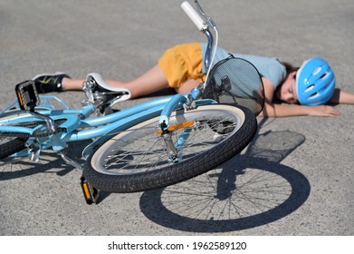 Young Girl Fallen Of A Bicycle Laying Down Beside Her Bike Unconscious On Paved Road. Real People. Copy Space