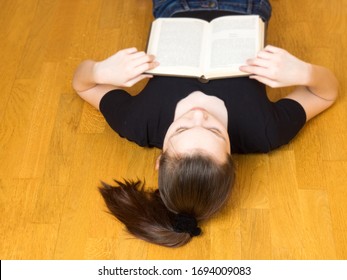 Young Girl Fell Asleep Reading A Book On A Brown Wooden Floor