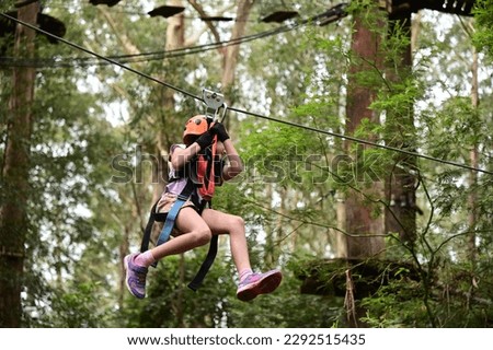 Young girl (female age 08) sliding on a flying fox zip line during a treetop adventure climbing. Girls power, risk and challenge concept. Real people. Copy space