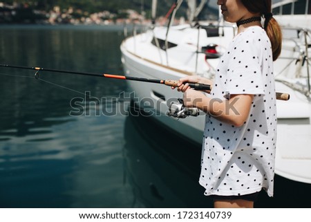 Young girl fishing near the shore after quarantine in white t-shirt. Summer time. 