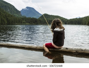 Young Girl Fishing Off Log Into Mountain Lake In Washington State