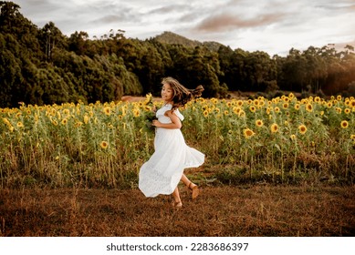 Young girl in flowy white dress dancing in field of sunflowers