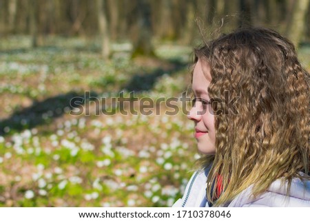 A young girl in the forest in a clearing with spring flowers