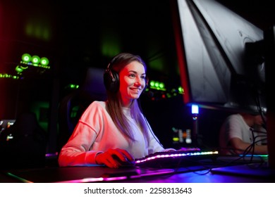 young girl gamer sits in headphones in a computer club looks at the monitor and smiles, portrait of a cybersports girl
