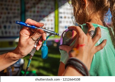 Young girl getting an airbrush stencil temporary tattoo in a family festival outdoors - Closeup picture with many different tattoo designs displayed in the blurry background
