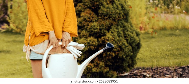 A young girl with gloves and rubber boots is going to water plants in her beautiful summer garden. A professional woman gardener with a watering can is irrigating her lawn and flowers. - Powered by Shutterstock