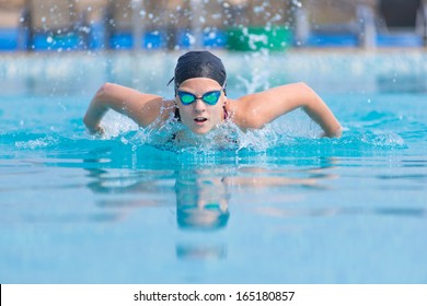 Young girl in goggles and cap swimming butterfly stroke style in the blue water pool