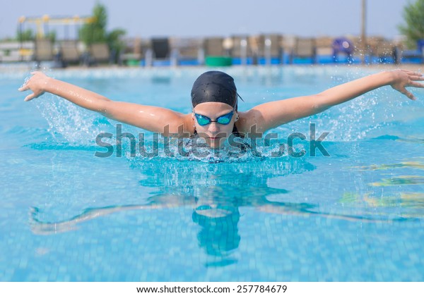 Young girl in goggles and cap swimming\
butterfly stroke style in the blue water\
pool