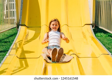 Young Girl Going Down Large Yellow Slide On A Hessian Bag At An Amusement Park, Carnival, Fairground.