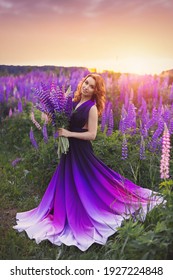 A young girl in gradient haute couture dress in black  purple   white colors standing among blooming lupine field at sunset 