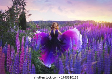 A young girl in gradient haute couture dress in black  purple   white colors standing among blooming lupine field at sunset 
