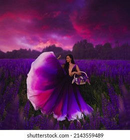 A young girl in gradient haute couture dress in black  purple  pink   white colors standing among blooming lupine field in the evening twilight 