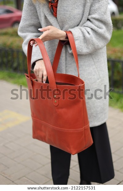 A young girl in a gray coat and a brown scarf is\
walking down the street, holding a large shopper bag in her hands.\
A bag for girls made of genuine leather. Beauty and fashion,\
accessories for women