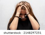 A young girl handcuffed on a gray background, close-up. Juvenile delinquent in a black T-shirt, criminal liability of minors.