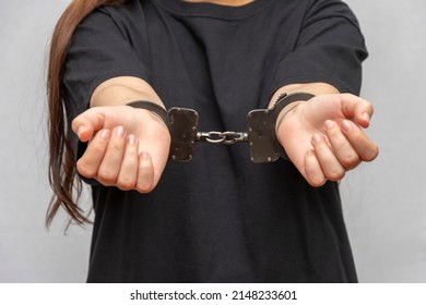 A Young Girl Handcuffed On A Gray Background, Close-up. Juvenile Delinquent In A Black T-shirt, Criminal Liability Of Minors.