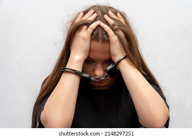 A young girl handcuffed on a gray background, close-up. Juvenile delinquent in a black T-shirt, criminal liability of minors. - Shutterstock ID 2148297251