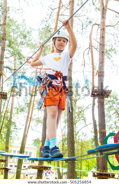 Young girl in harness climbing and trying\
facilities in an adventure\
park.