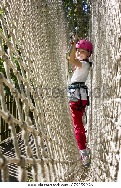 Young girl in harness climbing and trying\
facilities in an adventure rope\
park.