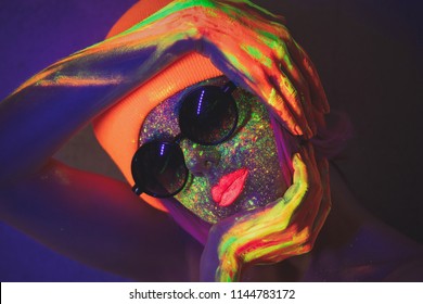 Young girl in hat with fluorescent paint on lips and face and sunglasses. Studio shot.