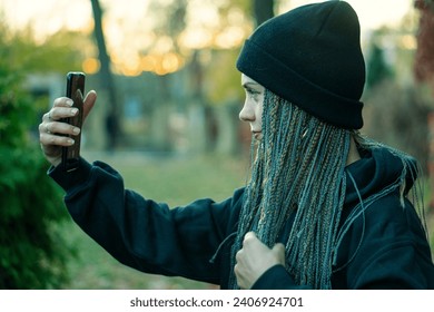 A young girl in a hat with a phone in her hands. A girl walks in the autumn park and uses a mobile phone. Portrait of a woman with a device. - Powered by Shutterstock