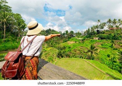 Young girl with hat pointing to the rice fields. Rice terraces famous place Tegallalang near Ubud. The island of Bali in Indonesia in Southeast Asia.