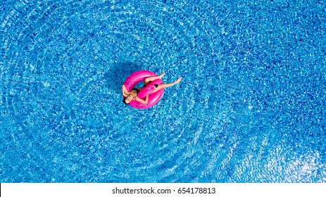 Young girl having fun and laughing and having fun in the pool on an inflatable pink flamingo in a bathing suit in summer from above