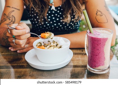 Young Girl Having A Good Morning Healthy Breakfast Smoothie Bowl  And A Drink Made Of Super Foods, Fruits, Nuts, Berries, Granola, Shredded Coconut, Acai