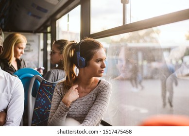 A young girl with headphones looks out the window of public transport and listens to music - Powered by Shutterstock