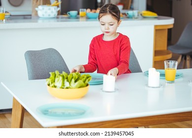 A Young Girl Helps To Set The Family Dining Room Table. Preschooler Kid Helping Mother To Set Table In Kitchen, Carrying The Plates, Kitchen Interior. 