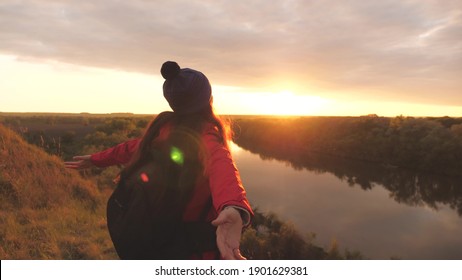 A young girl with her arms outstretched feels freedom in the sunset. Woman adventurer on the background of the sky. Research work with a backpack. Weekend hike. Tourist on the ground. Life joy in