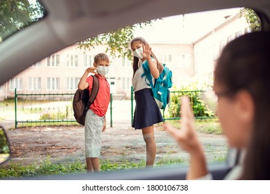 Young Girl And Her Brother In Medical Masks With Backpacks Waving Goodbye To Their Parents To The Car While Going To School During The Pandemic