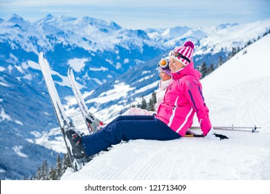 Young girl with her mother in a ski outfit sitting on the snowy hill in the Zillertal Arena, Austria