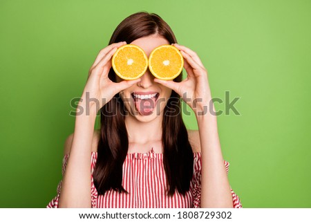 Young girl hold two orange slices stick tongue isolated green color background