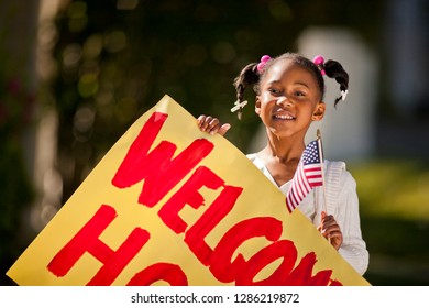 Young Girl Holding An American Flag And A Welcome Home Sign.