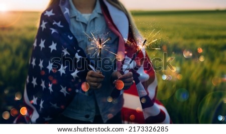 Young girl holding Bengal fire with American flag at sunset. America celebrate 4th of July. Independence Day.
