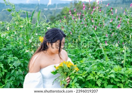 Young girl holding the bushes of wild sunflower bloom in yellow in flower field.