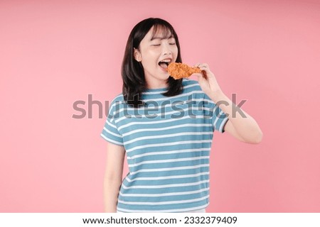 Young girl holding, eating fried chicken isolated on pink background