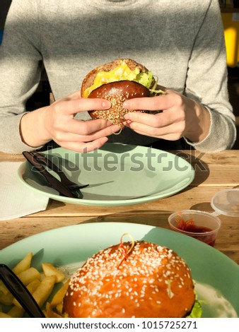 Young girl holding in female hands fast food burger. Hungry person smiling with grilled hamburger