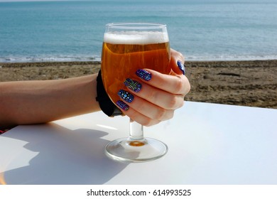Young girl holding a glass of beer in hand with beautiful and colorful nails