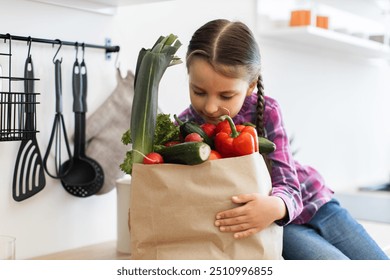 Young girl holding grocery bag filled with fresh vegetables in kitchen. Healthy lifestyle, home cooking, and nutrition concept. Child exploring fresh produce. - Powered by Shutterstock