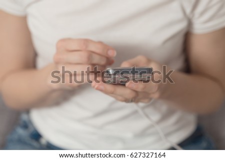 Young girl holding her phone and texting; phone connected to charger, effect applied in post processing