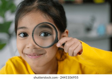 A young girl is holding a magnifying glass and looking at something. She is smiling and she is curious about what she is looking at - Powered by Shutterstock