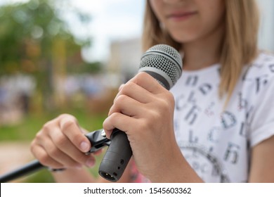 Young Girl Holding Mic With Two Hands. Microphone And Unrecognizable Girl Singer Close Up. Cropped Image Of Female Teen Singer In The Park. Copyspace