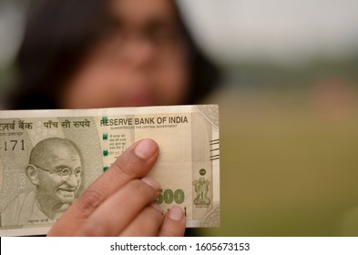 A Young Girl Holding A New Green 500 Rs Indian Currency Note In Her Hand Issued After Demonetisation In A Park With A Green Background Pointing To Reserve Bank Of India Written On The Note