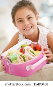 Young Girl Holding Packed Lunch In Living Room Smiling