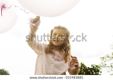 Young girl holding pink balloons in the air and smiling in the park.